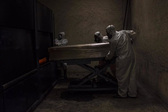 Un grupo de sepultureros acarrea con el ataúd de una víctima de coronavirus una vez ha finalizado el acto religioso en su memoria.