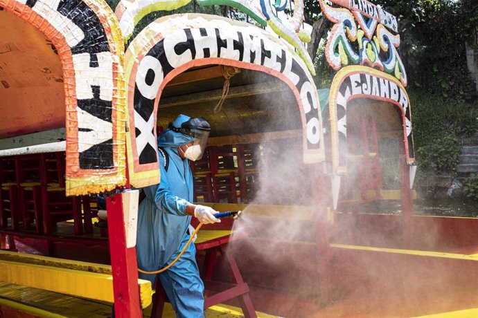 Un trabajador con traje protector desinfecta las coloridas embarcaciones de Xochimilco, en Ciudad de México, mientras el popular lugar turístico se prepara para reabrir este sábado.