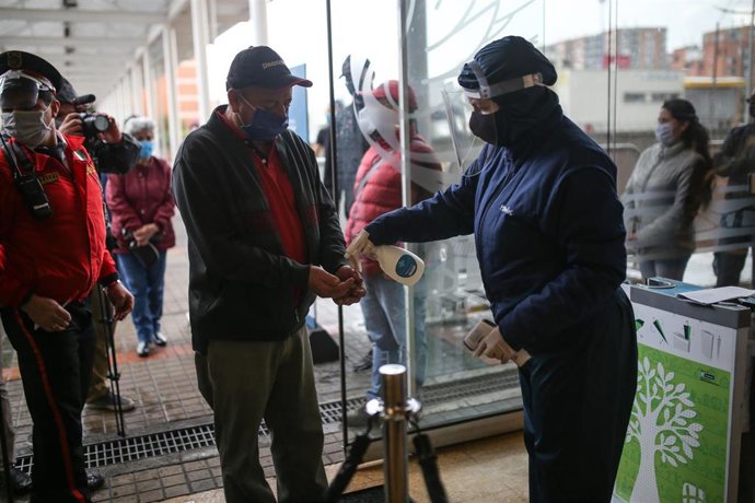 Una personas es rociada con gel desinfectante antes de ingresar en eun centro comercial de Bogotá, Colombia.
