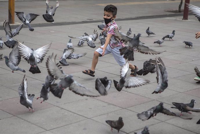 Un niño con mascarilla espanta a unas palomas en Teherán