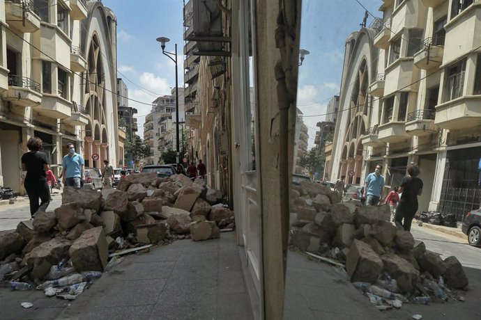 Personas reflejadas en un espejo junto a un edificio dañado por la explosión en Beirut