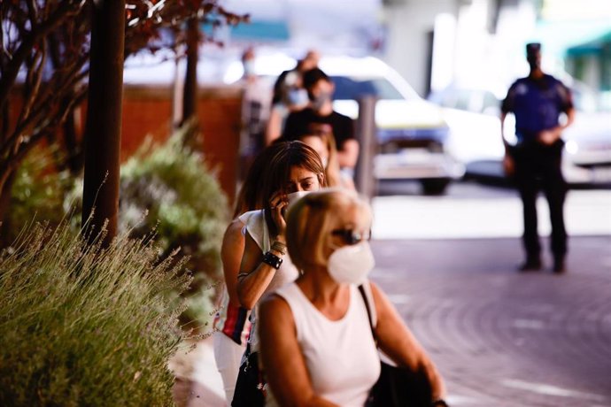 Varias personas protegidas con mascarilla esperan sentadas en las inmediaciones donde durante la jornada de hoy realizarán PCR aleatorias a personas de entre 15 a 49 años, a la que han sido convocados 1.500 vecinos de Villaverde, Madrid, (España), a 19 