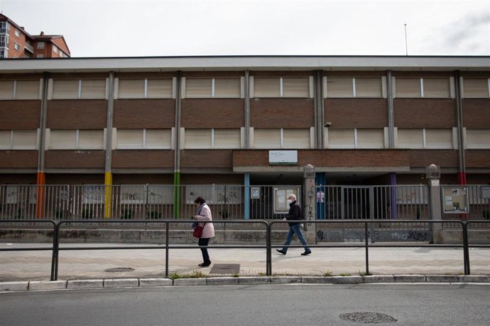 Un hombre con mascarilla y una mujer pasan frente a un colegio cerrado, en Vitoria / País Vasco (España)