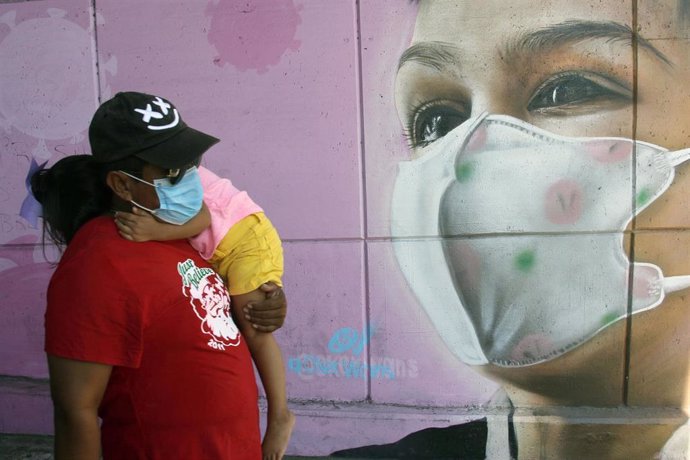 Una mujer camina por delante de un mural con mascarilla por el coronavirus en México.
