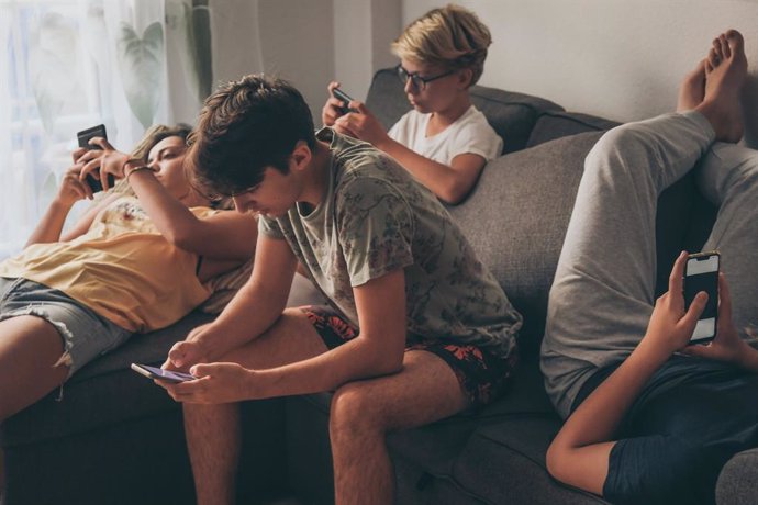 Grupo de adolescentes sentados mirando sus móviles.