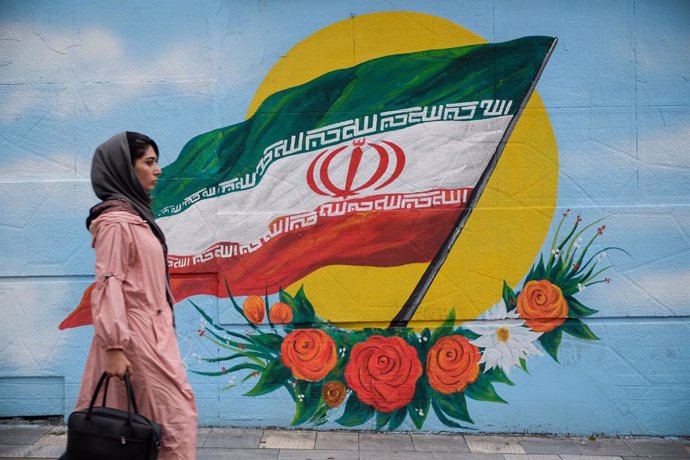 Una mujer camina frente a un mural con la bandera de Irán situado en una de las 
