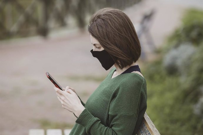 Una mujer con mascarilla utiliza un teléfono móvil