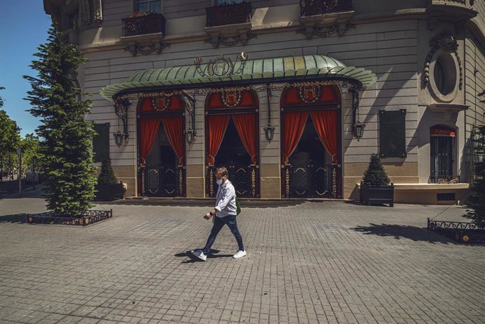 24 April 2020, Spain, Barcelona: A man wearing a face mask passes the closed hotel "El Palace" amid the nationwide lockdown due to the coronavirus crisis. Photo: Matthias Oesterle/dpa