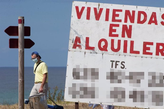 Un hombre camina junto a un cartel de viviendas en alquiler.