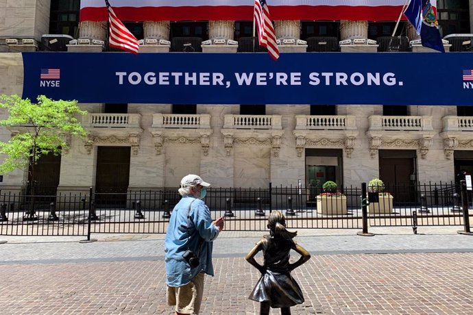 Un hombre con mascarilla junto a la estatua frente a Wall Street