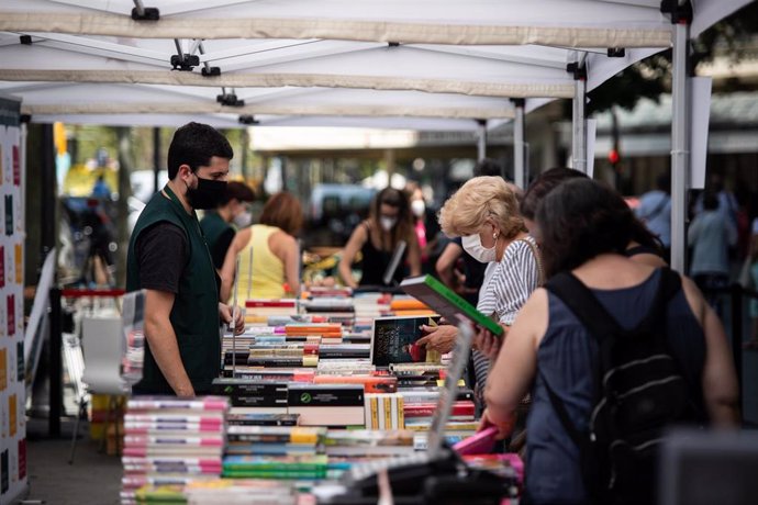 Varios personas observan libros en varios puestos de libros colocados en la calle, en Barcelona, Catalunya (España), a 23 de julio de 2020. 