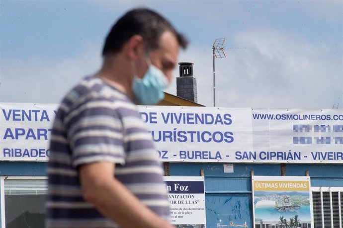 Un hombre camina junto a un cartel de viviendas en venta en A Mariña (Lugo/Galicia) a 26 de julio de 2020. La comarca mantiene este domingo 51 casos activos de COVID-19 tras una nueva alta y un nuevo contagio con respecto al sábado.