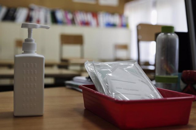 Mascarillas y gel desinfectante en la mesa del profesor de un aula donde se pueden observar los pupitres colocados y separados entre sí para el nuevo curso del colegio Virgen de Europa, debido a las nuevas medidas de distanciamiento que se han de tomar pa