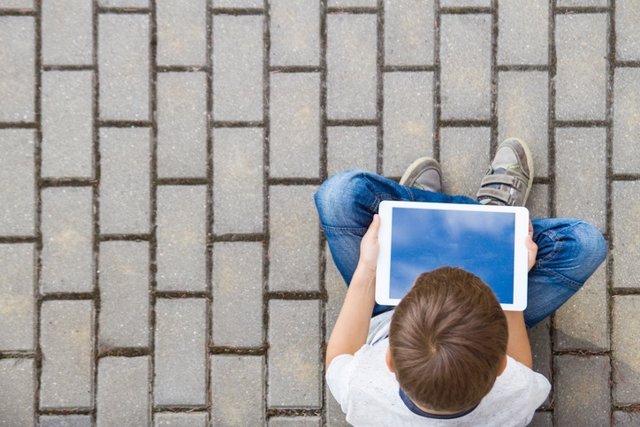 Child with tablet computer sitting outdoors. Education, learning, technology, friends