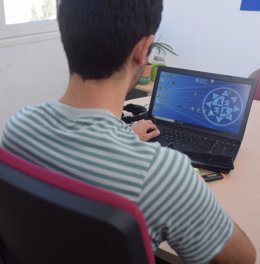 Imagen adjunta de un joven viendo en un portátil un vídeo docente de la UPCT.
