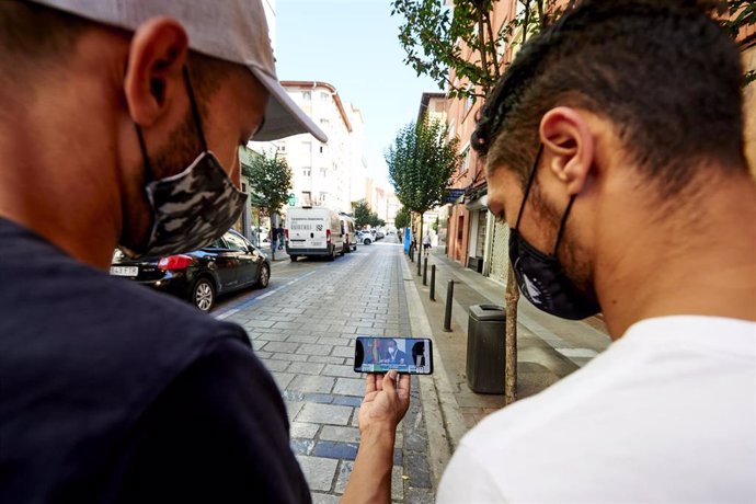 Dos personas observan desde su móvil las noticias en una de las calles del barrio La Inmobiliaria de Torrelavega