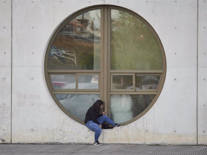 Una estudiante consulta su móvil junto a una ventana de la UPNA