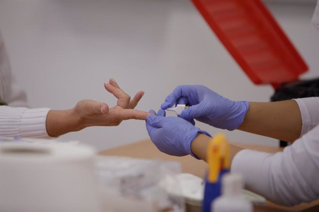 Personal sanitario de Cruz Roja saca sangre de un dedo a una persona para realizar el test rápido de detección de anticuerpos IgG e IgM