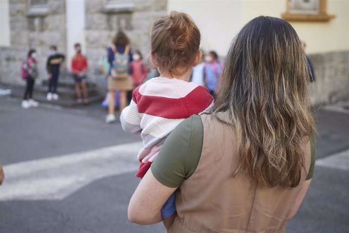 Una madre carga con su hija en el patio del Colegio Público Víctor Pradera en el primer día de colegio del curso escolar 2020-2021 en Pamplona
