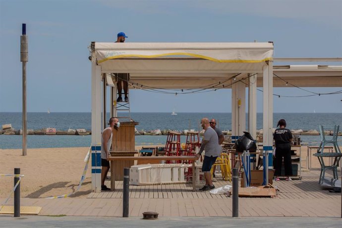 Varios trabajadores preparan la terraza de un bar junto a la playa durante el segundo día de la reapertura al público de las terrazas al aire libre de los establecimientos de hostelería y restauración limitándose al 50% de las mesas y garantizándose una