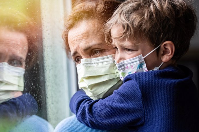 Covid-19, mujer y niño con mascarilla mirando por la ventana.