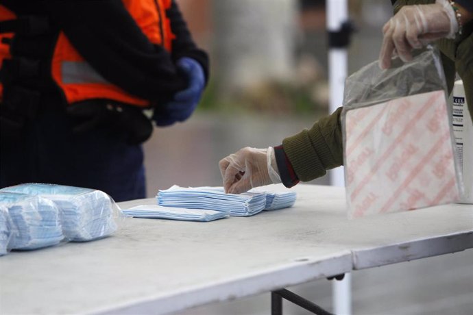 Transeúntes recogen mascarillas puestas a disposición de viajeros y usuarios de transporte público en las inmediaciones de la estación Intermodal.