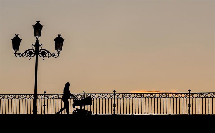 Una madre con un carrito de bebe paseando al atardecer  por el Puente de Triana