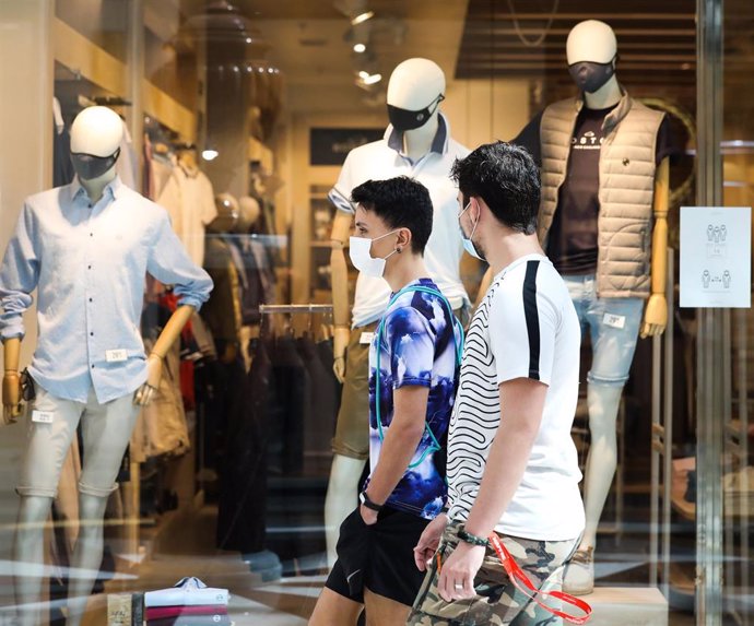 Dos jóvenes pasan junto a una tienda de ropa del Centro Plaza Norte 2, La Cúpula de Madrid. 