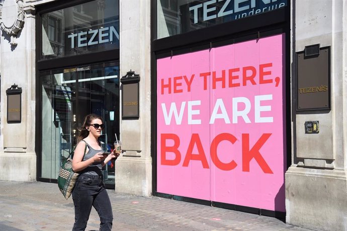 14 June 2020, England, London: A woman passes signage indicating a store is re-opening on Oxford Street, ahead of the re-opening of non-essential retailers in England on 15 June as part of the easing of the Coronavirus (Covid-19) lockdown restrictions. 