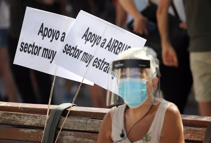 Una mujer protegida con mascarilla y pantalla sentada en un banco donde hay dos carteles en los que se puede leer "Apoyo a Airbus, sector muy estratégico" durante una manifestación de los empleados de Airbus en Getafe (Madrid) el pasado 23 de julio