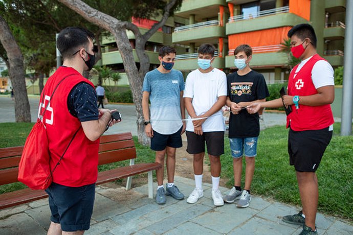 Pla general de dos voluntaris de la Creu Roja marcant la distncia mínima de seguretat amb un metre a uns joves a Platja d'Aro el 23 de setembre de 2020 (Horitzontal)