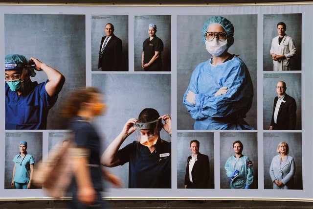 Una persona con mascarilla pasa delante de una exhibición fotográfica con imágenes de trabajadores sanitarios en Melbourne