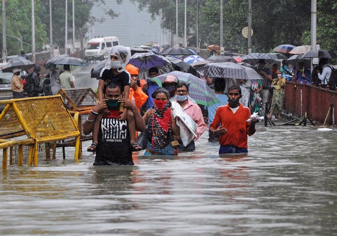 Personas con mascarilla en una zona inundada por las fuertes lluvias en Bombai