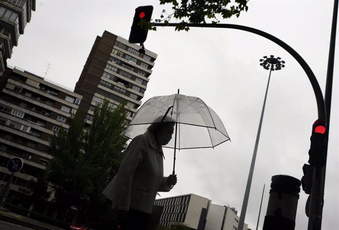 Una mujer pasea con un paraguas en la capital en un día de lluvia y bajada de temperaturas en toda España.