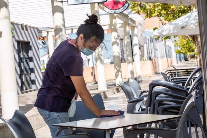 Una camarera limpia una de las mesas de la terraza de un bar.