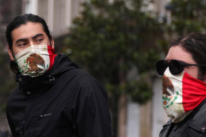 Dos personas se cubren la boca con sendos pañuelos con la bandera mexicana.
