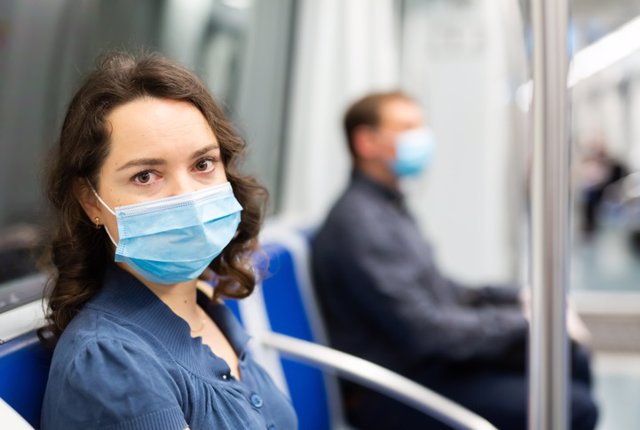 Brunette in medical mask in subway car    Young brunette in medical face mask and protective gloves riding in modern subway car. Concept of forced city trip in context of coronavirus pandemic
