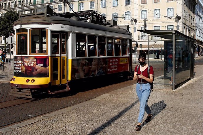 Una mujer con mascarilla junto a un tranvía en Lisboa