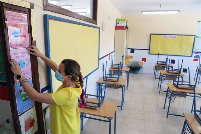 Una profesora coloca carteles de medidas preventivas ante el COVID-19 en el aula antes del inicio del curso escolar en un colegio público