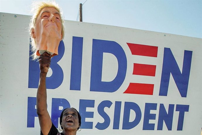 Una mujer con una mascara de Donald Trump ante un cartel de Joe Biden