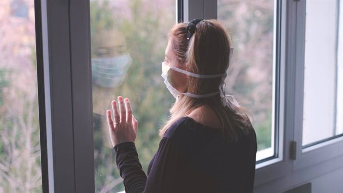 Mujer con mascarilla mira a través de una ventana.