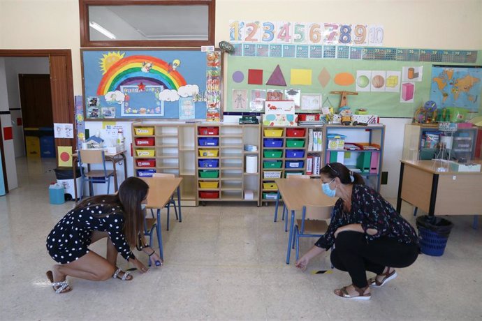 Dos profesoras del colegio público Pablo Neruda, en Málaga, miden la distancia entre bancas en el aula infantil como medidas preventivas ante el COVID-19