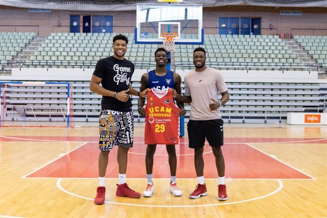 Giannis Antetokounmpo (izda) junto a sus hermanos Alex y Thanasis sujetando una camiseta del UCAM