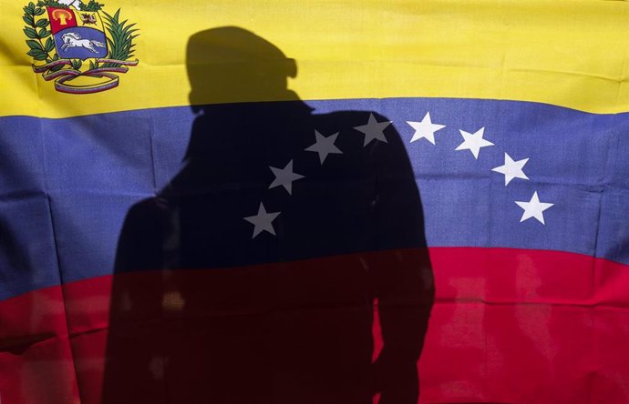 Un hombre detrás de una bandera de Venezuela.