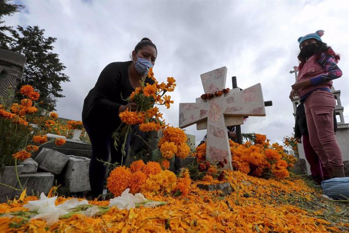 Una persona deposita una ofrenda floral en la tumba de un familiar fallecido a causa de la COVID-19.