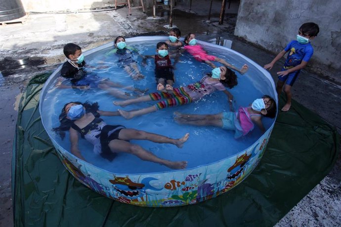Niños con mascarilla bañándose en una piscina desmontable en Gaza