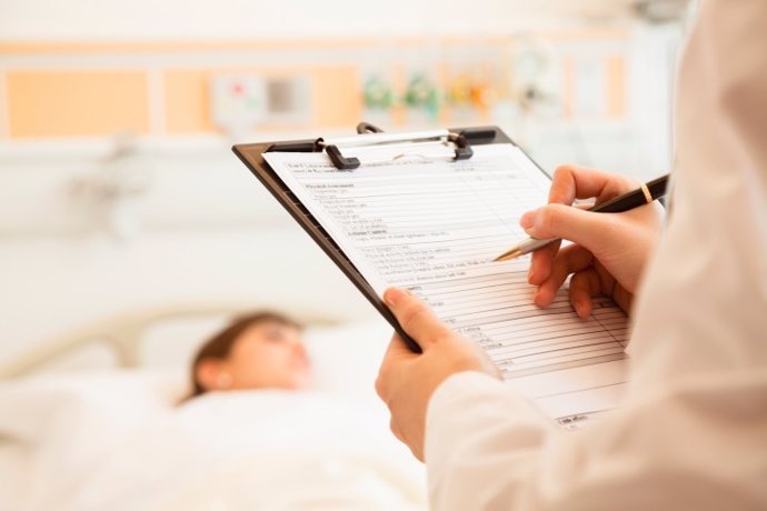 Close-up of doctor writing on a medical chart with patient