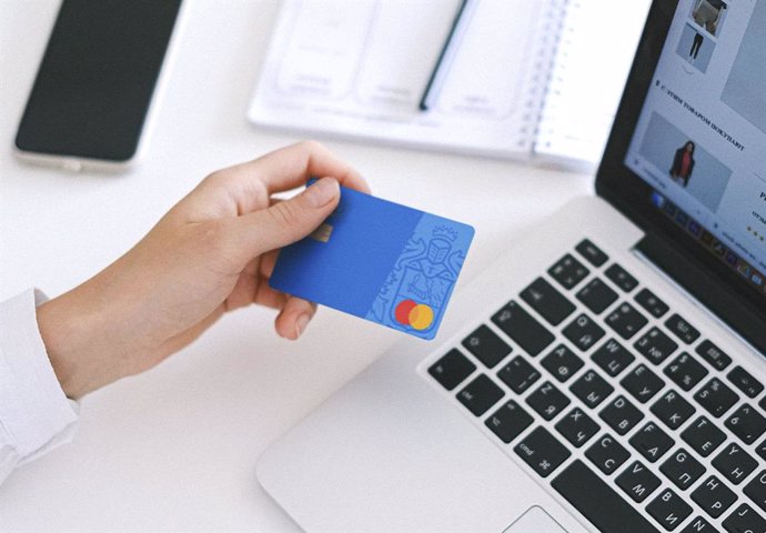 Una persona utilizando su tarjeta de crédito para realizar compras online con un ordenador
