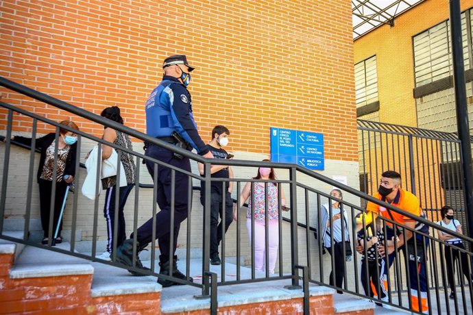 Un agente de la Policía Municipal pasa junto a varias personas que esperan en una cola en el centro cultural El Pozo 