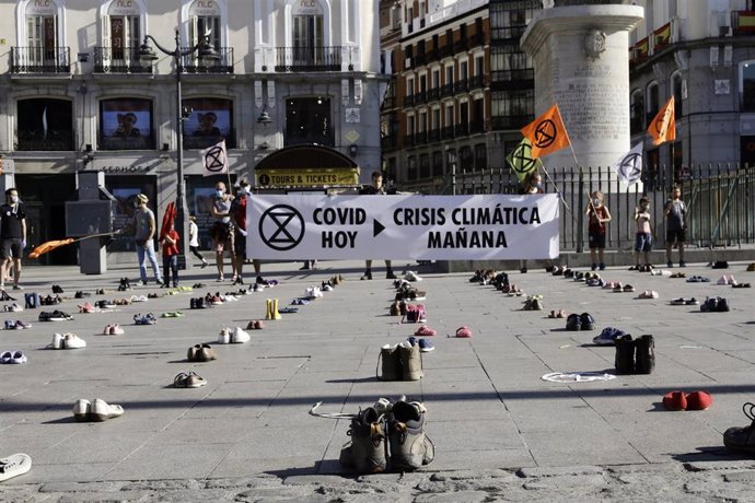 Activistas sostienen pancartas en las que se lee 'Covid hoy, crisis climática mañana, actuad YA', en la Puerta del Sol de Madrid, que aparece cubierta de zapatos, en una iniciativa del movimiento internacional de desobediencia civil pacífica Extinction 